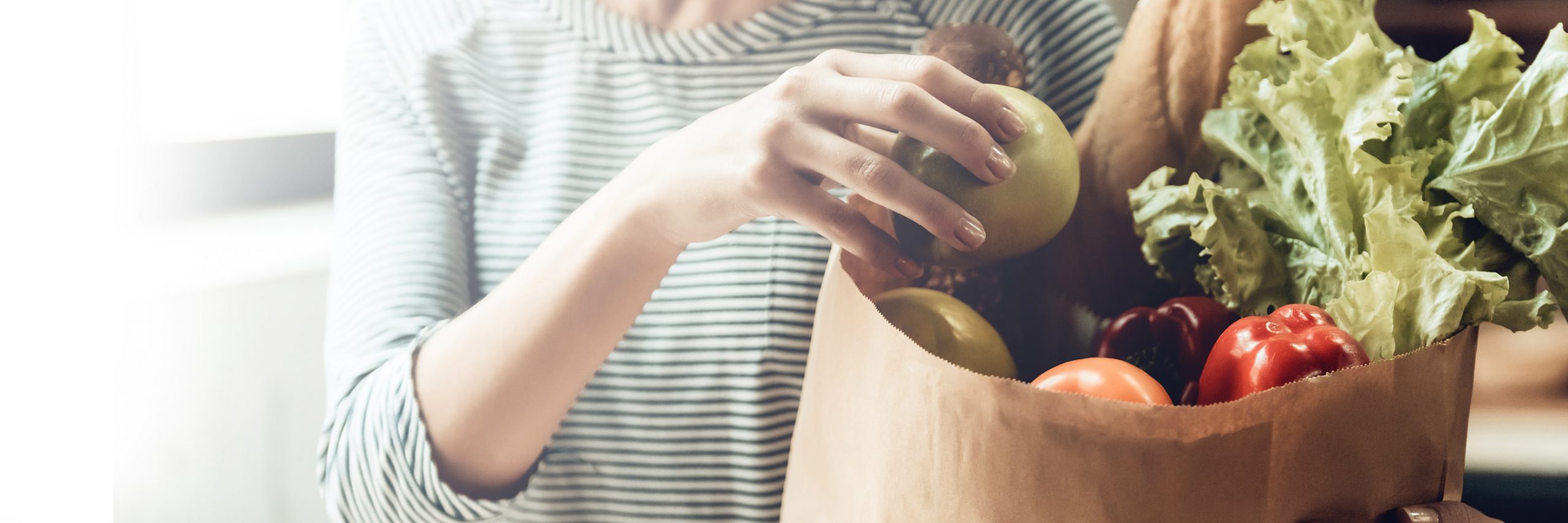 Woman placing groceries in a brown paper bag